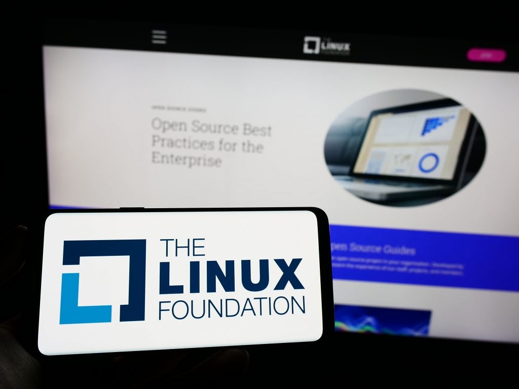The Linux Foundation logo on a smartphone screen, with a blurred background featuring a website about &quot;Open Source Best Practices for the Enterprise.